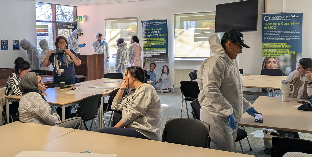 People in a classroom, some wear white hazmat suits.