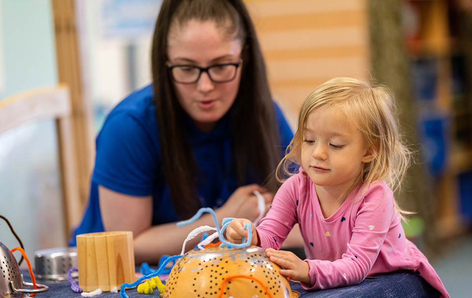 Young nursery worker teaching and caring for infant child