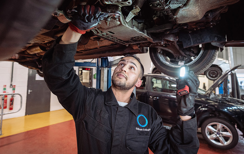 Male student working on the underneath of a car that is on the ramp