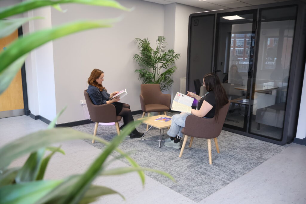 Two people sit on chairs in a meeting area and read magazines